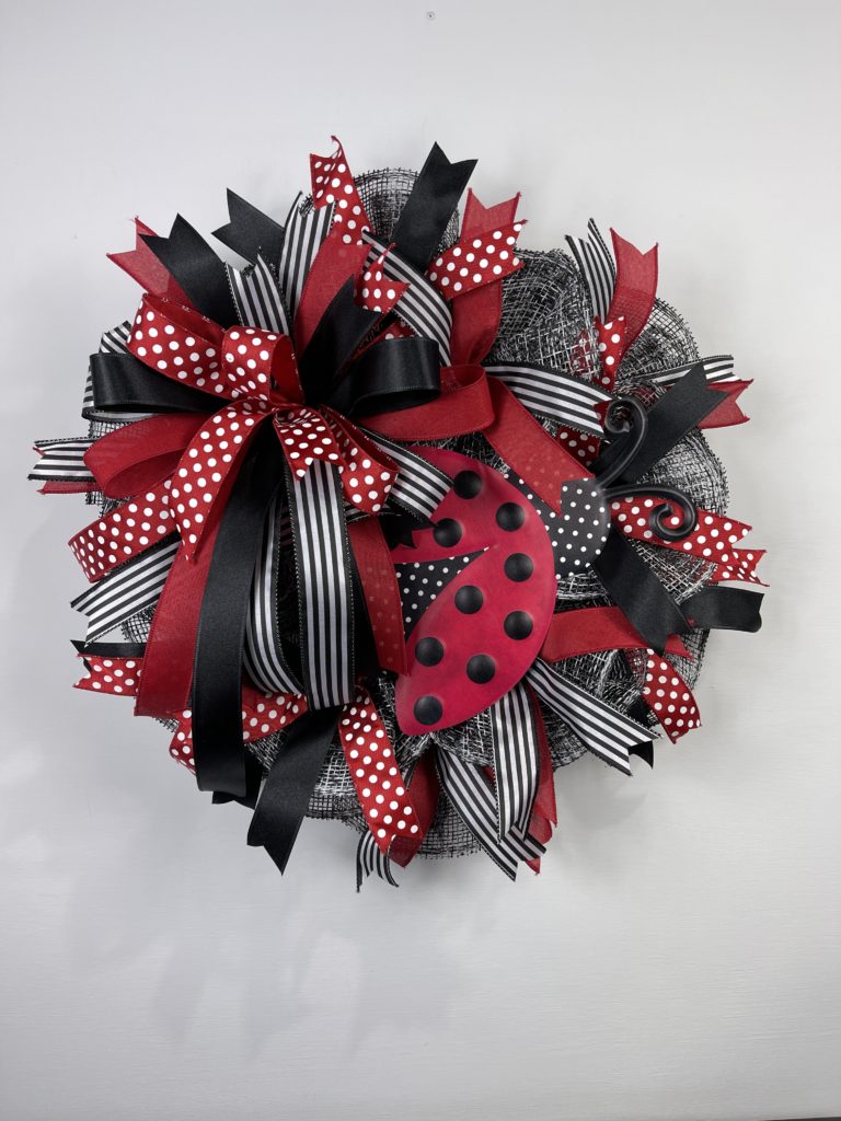 wreath with black and white mesh, black, red, and white ribbon, and a ladybug wreath attachment