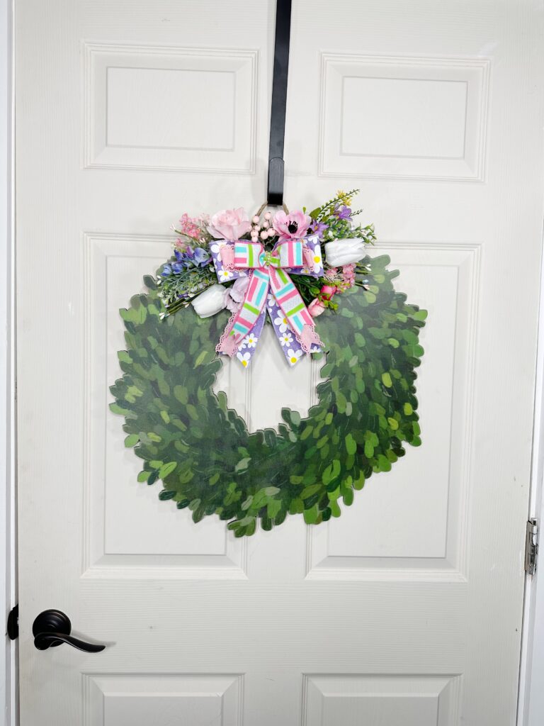 Full view of the entire door with the floral wreath centered. The door hanger displays the vibrant bow and pastel spring florals in a symmetrical and cheerful design.