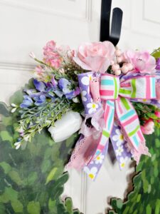 Close-up of the left side of the bow and surrounding florals, showcasing layered purple and white blooms, soft pink roses, and white tulips among wispy greenery.