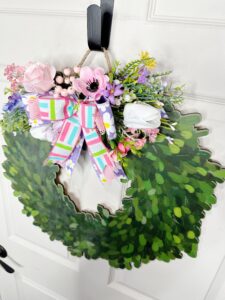 Top angle of the floral wreath, showing a full arrangement of lush greenery and mixed florals. The ribbons cascade down the center, adding a playful pop of color.