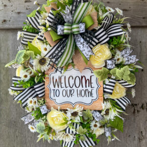 Oval wreath with with welcome to our home sign, flower blooms, and ribbon.
