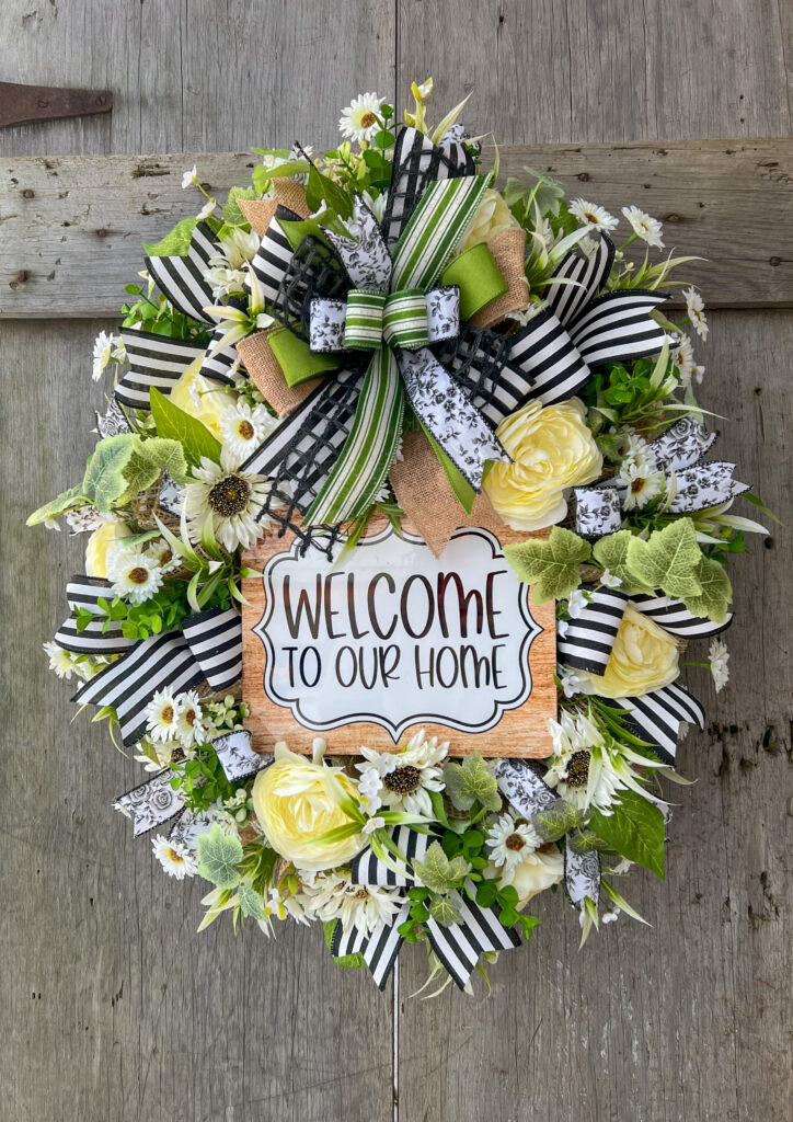 Oval wreath with with welcome to our home sign, flower blooms, and ribbon.