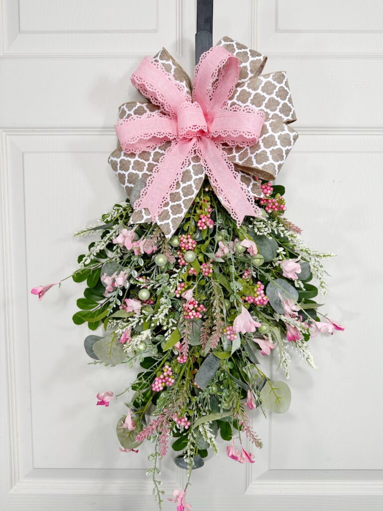 Full view of the completed pink and green berry swag, showing a cascading floral arrangement with pink berries, greenery, and a two-ribbon bow at the top.